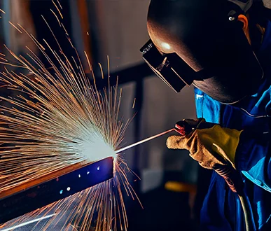 FLYZONE Engineering welder performing high-precision arc welding on a metal beam, with bright sparks flying in a controlled fabrication environment.